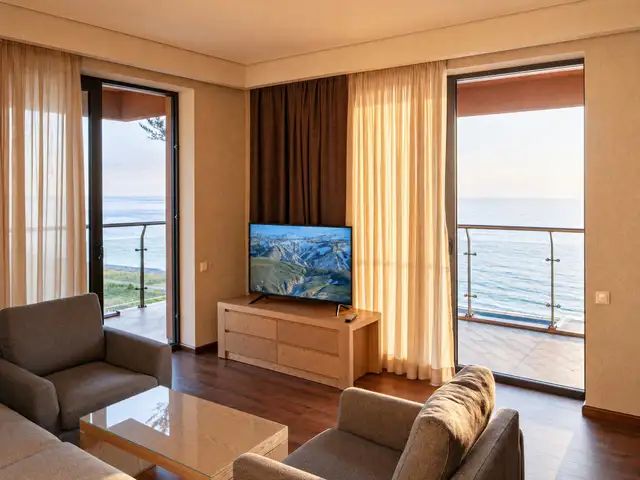 Living room with mounted TV and twin balcony doors framing the sea